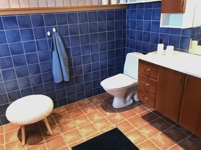 a blue tiled bathroom with a toilet and a stool at Seaside 3-bedroom House in Svelgen