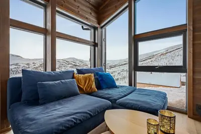 a living room with a blue couch in front of windows at Ski in ski out mountain cabin with views and extra unit option in Sogndal