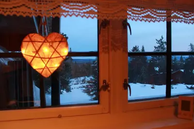 a heart ornament hanging in a window with a winter view at Hytte sentralt Ljøsheim, Ringsaker(nær Sjusjøen) in Ringsaker