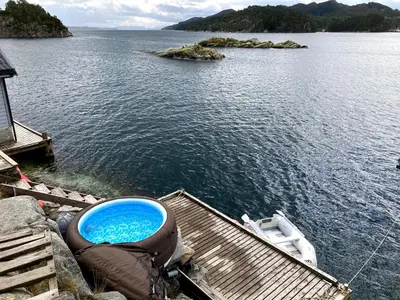 a boat sitting on a dock next to a body of water at Bergen/Sotra: Sea cabin. Spa. Fishing. Boat in Haganes