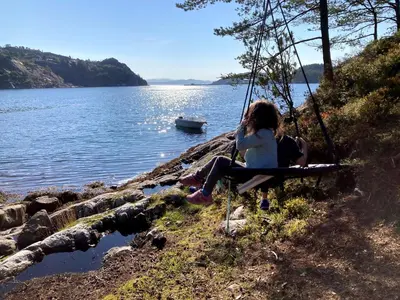 a girl sitting on a swing by a lake at Bergen/Sotra: Sea cabin. Spa. Fishing. Boat in Haganes