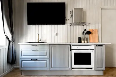 a kitchen with white cabinets and a tv on the wall at VILLA BRATTHOLMEN in Brattholmen