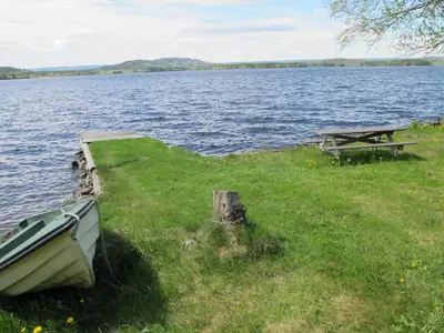 a picnic table and a boat on the grass next to a lake at Festly in Ringsaker