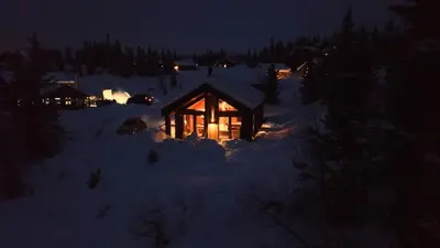 a lit up log cabin in the snow at night at Unique cabin with fantastic lake view, sauna, ski & EV outlet in Svingvoll