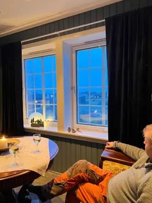 a man sitting at a table in a room with windows at Sjarmerende hus med veldig stort uteareal. in Brekstad