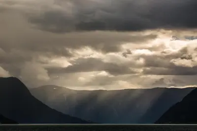 a cloudy sky with mountains and a body of water at Lyngmo Gjestehus in Hafslo
