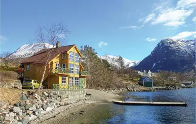 a yellow house next to a river with snow covered mountains at Cozy Apartment In Rosendal in Rosendal