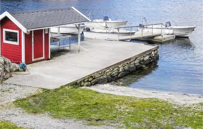 a dock with a red house and boats on the water at Amazing Home In Nordtveitgrend in Hjartåker
