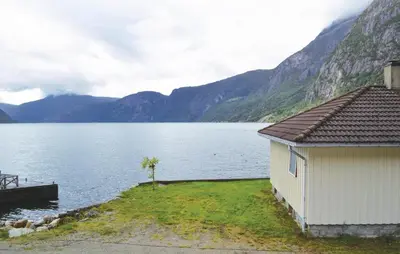 a building next to a body of water with mountains at Holiday Home Eidfjord Simadalsv in Eidfjord