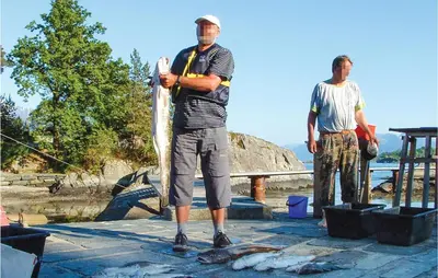 two men standing on a dock holding a fish at Lovely Home In Hatlestrand With Kitchen in Hatlestrand