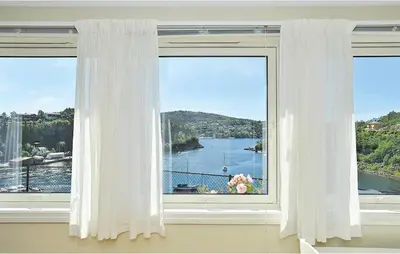 a window with white curtains and a view of the water at Cozy Apartment In Straumsgrend in Bergen
