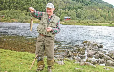 a man standing next to a river holding a fish at Stunning Home In Sogndal With Sauna in Sogndal