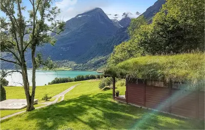 a house with a grass roof with a lake and mountains at Flåten Hyttegrend in Olden