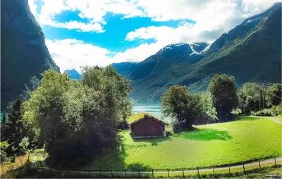 a barn in a field with a lake and mountains at Flåten Hyttegrend in Olden