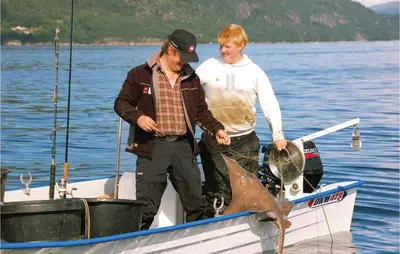 two men standing on a boat with a shark on it at Hytte 19 in Ikornnes