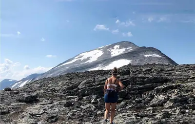a woman standing on a rocky mountain with a snow covered mountain at Solhavn in Eidsvåg