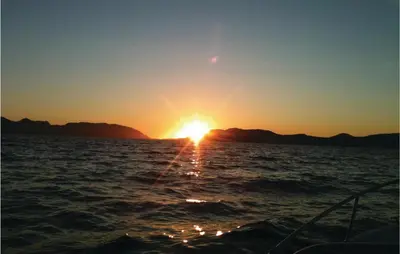 a sunset on the water with a boat at Lovely Home In Vågstranda in Hjelvik