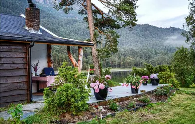 a woman sitting at a table outside of a house with flowers at Lovely Home In Bjoa With Kitchen in Utbjoa