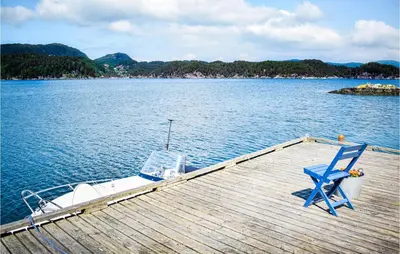 a dock with a blue chair and a boat on the water at Gorgeous Home In Reksteren With Kitchen in Klinkholmen