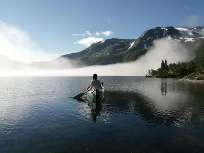 a man is sitting in a canoe in the water at Reinunga Eco Hytta - Mountain lodge near Myrdal accessible only by train or bike in Myrdal