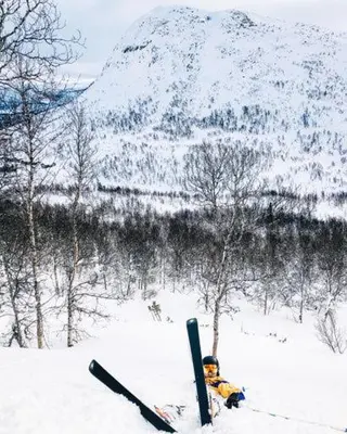 a person laying in the snow next to a snow covered mountain at Lisletun in Hovden
