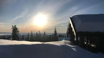 a snow covered building with the sun in the background at Berghstua - Natrudstilen på Sjusjøen in Sjusjøen