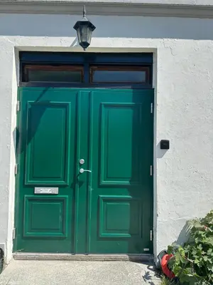 a green door on a white building with a light above it at Apartment «Ladegården» in Bergen in Bergen
