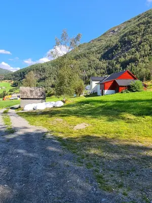 a gravel road next to a red barn and a mountain at Jondal Nice apartment with bed linen incuded in Jondal