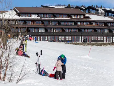 a man and a child standing in the snow in front of a lodge at Bergo Leiligheter in Beitostøl