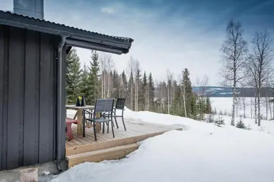a wooden deck with a table and chairs in the snow at Nærglimt - cabin by the lake Næra in Ringsaker