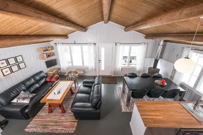 a living room with black leather furniture and wooden ceilings at Nærglimt - cabin by the lake Næra in Ringsaker