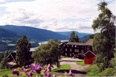 a large building on a hill with mountains in the background at Glomstad Gjestehus in Tretten