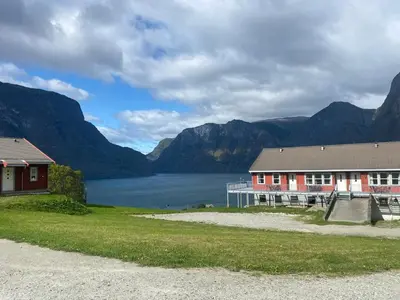 a building next to a body of water with mountains at Winjum Hostel Stegastein in Aurland