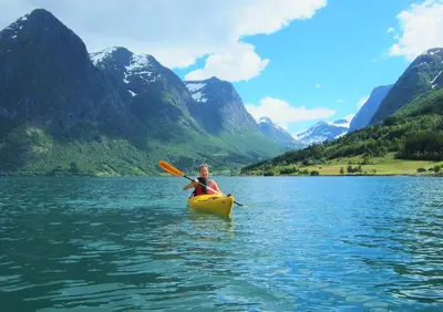 a person in a kayak on a lake with mountains at Nesje Gardstun in Oppstryn
