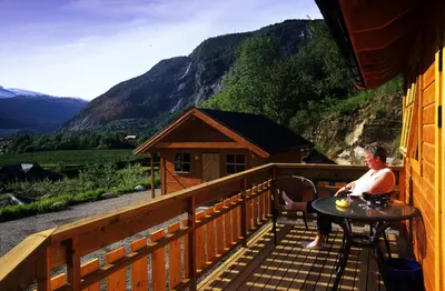 a woman sitting at a table on the balcony of a cabin at Gaupnetunet Hotell og Hytter in Gaupne