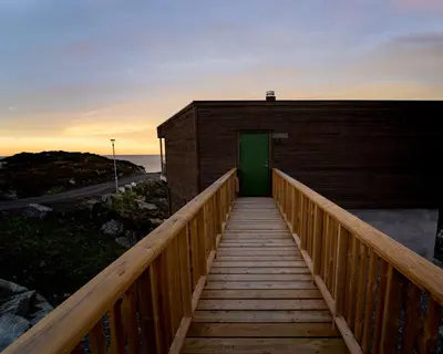 a wooden boardwalk leading to a green door on a building at Runde Panorama - Ørneredet in Runde