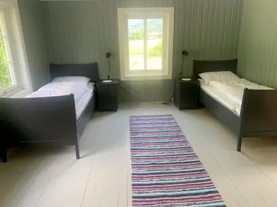 two beds in a room with two windows and a rug at Engen Gård in Innfjorden
