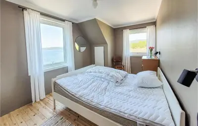 a bedroom with a large bed with two windows at Nice Home In Fitjar With House Sea View in Fitjar