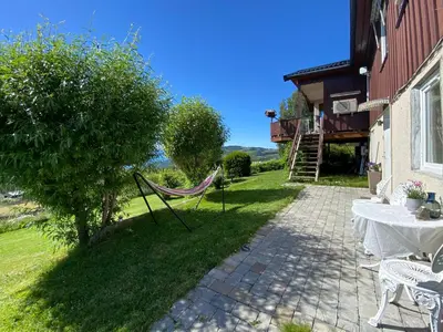 a patio with a table and a hammock next to a building at Landlig beliggenhet med flott utsikt over Mjøsa in Ulven