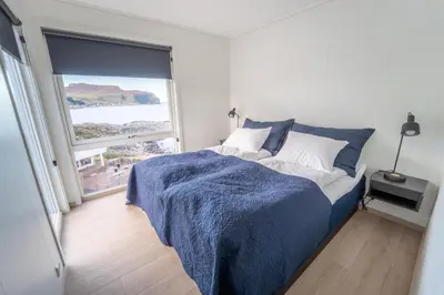 a bedroom with a bed with a blue blanket and a window at Runde Panorama - Trollvogga in Runde