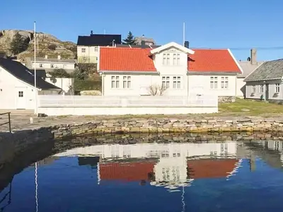 a house with red roofs is reflected in a body of water at 6 person holiday home in Hernar-By Traum in Bøvågen