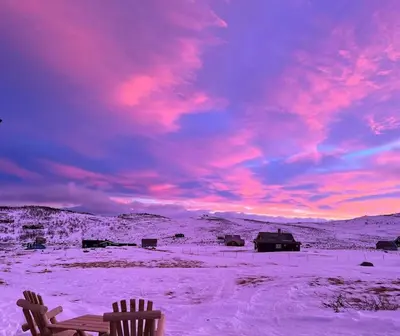 a sunset in a snow covered field with a bench at Seterhytte i Havsdalen in Geilo
