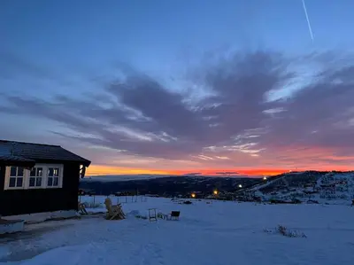 a house in the snow with a sunset in the background at Seterhytte i Havsdalen in Geilo
