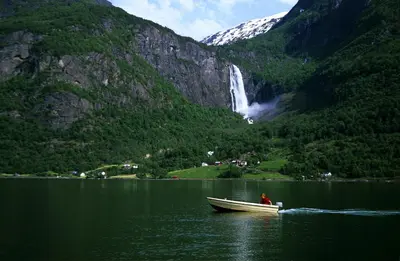 a boat in a body of water with a waterfall at Pluscamp Sandvik in Gaupne