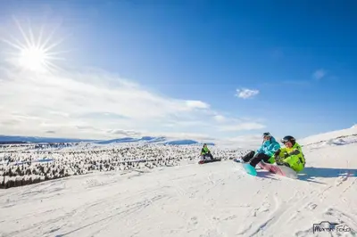two people sitting on a snowboard on a snow covered slope at Flott fritidsleilighet i Bualie på Golsfjellet in Gol