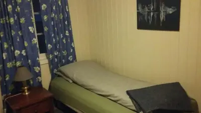a small bedroom with a bed with a blue curtain at Flemsøy in Ålesund