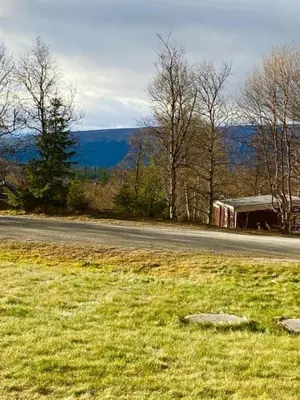 a road next to a field of grass and a building at Leilighet Beitostølen sentrum, terrasse og innendørs parkering in Beitostøl