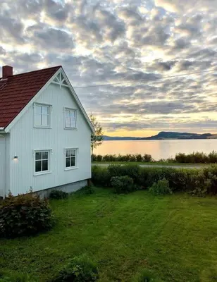 a white house in a field next to a body of water at The Fjord House in Snofugl