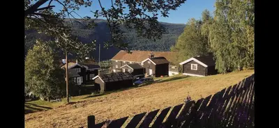 a house on a hill next to a fence at Traditional timber farm with Sauna & Wi-Fi in Baukål