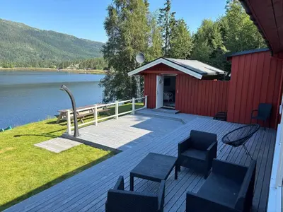 a deck with chairs and a red building next to a lake at 9 person holiday home in Mosvik-By Traum in Mosvik